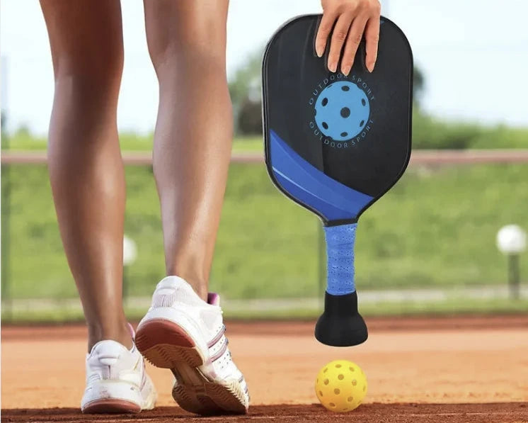 Pickleball player using paddle with attached suction cup to pick up yellow ball on court